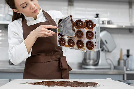 厨师或巧克力师在专业厨房制作甜巧克力 她把模具翻过来 把剩下的巧克力倒在桌子上糖果商业女士生产面包面包师糕点美食食物烘烤图片