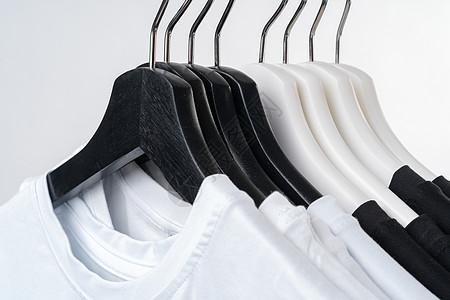 黑色和白色 T 恤挂在金属架上的衣架上 与白色隔离衣服配饰贮存销售精品家庭衣帽间房子库存衣柜图片