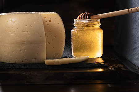 奶酪头放在生锈表面上的石板盘上 附近是一个染色的蜂蜜罐 里面装有 一块被麻子切成薄片的奶酪 水平方向图片