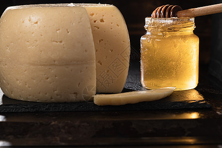 奶酪头放在生锈表面上的石板盘上 附近是一个染色的蜂蜜罐 里面装有 一块被麻子切成薄片的奶酪熟食奶制品美食小吃盘子产品乡村黄色食物图片