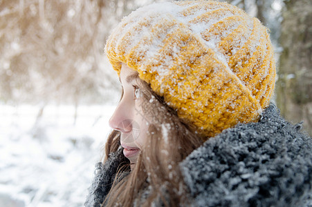 在雪林背景下 一位微笑着的年轻天主教女画像 戴着明亮的羊毛帽和围巾帽子女士女性针织帽女孩森林天气衣服羊毛图片