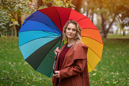 站在彩虹色雨伞下的公园里的年轻女子 一个漂亮的女孩在雨天穿过秋天的公园拥抱女朋友配件衣服树木女性幸福天气男朋友乐趣图片