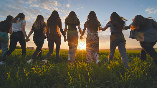 一群女孩在日落时手牵手朝太阳走去孩子幸福帽子女士天空橙子背包游客季节家庭图片