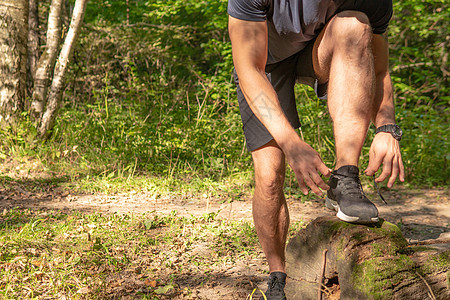 这位运动员正在用运动鞋系上他腿的鞋带 运动员在户外的公园里跑步 在森林周围 橡树绿草年轻持久的运动员运动自然 锻炼户外训练人员公图片