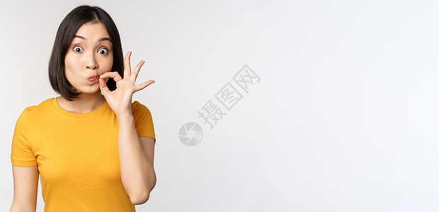可爱的亚裔女孩海豹嘴唇 用手指拉住嘴巴 承诺保守秘密 禁忌姿态 穿着黄色短袖圆领汗衫站在白色背景上大学互联网衬衫女士女朋友工作室图片