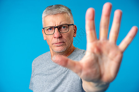 中年年年高龄蓝背景男子用手掌做停牌标记图片