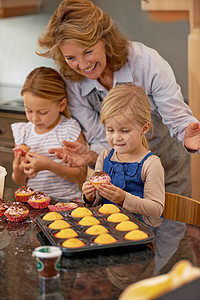一个祖母和她的两个孙子 在家里装饰纸杯蛋糕的 -你觉得呢?图片