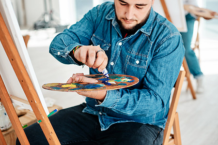 一位英俊年轻艺术家在摄影棚的艺术课上 将涂料挤到调色板上 拍到了一张照片图片