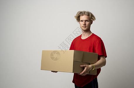 年轻送货员穿着红色T恤快乐地站立着 包裹是白色的 在白色背景上被隔开服务顾客船运邮递员邮件男性职业纸板男人邮差图片