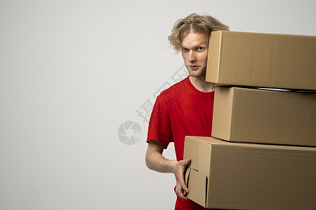 穿红色制服的年轻送货员拿着一堆纸板盒 运送邮包 包裹在白色工作室背景上 注 请看照片纸板货物男人邮件工人信使商业导游顾客命令图片