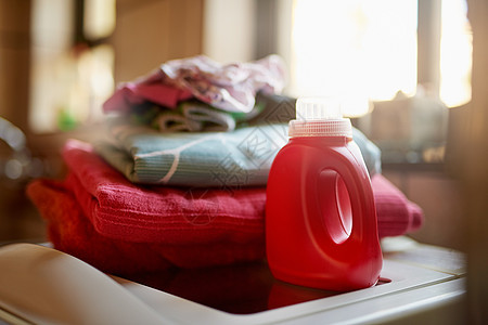 保持衣物清洁 一瓶洗涤剂和洗衣机顶部的一堆衣物的照片图片