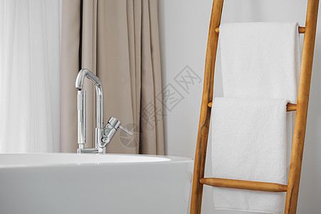 现代洗手间有现代浴缸 金属水龙头和装饰性木制楼梯上的白色毛巾图片