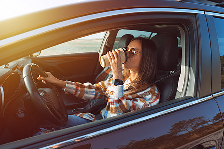 年轻时尚的女士驾着她的新车 在阳光明媚的一天喝咖啡;租车概念图片