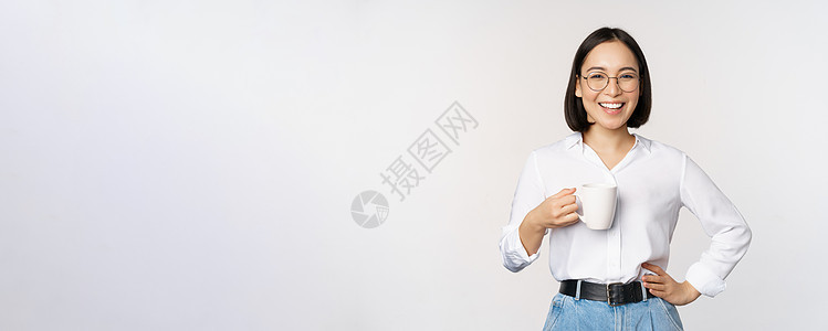 快乐的年轻精力充沛的亚洲女人微笑 喝酒 拿着咖啡杯杯杯子 在白色背景下自信地站立技术人士咖啡管理人员手臂成人女性售货员标识商务图片