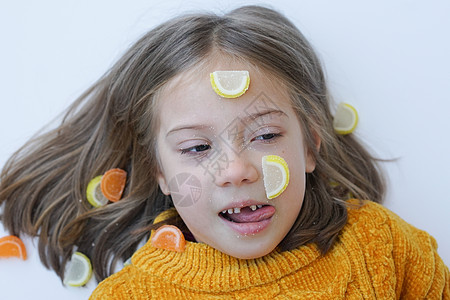 一个小女孩的肖像 与糖果躺在地板上 和毛发在黄色毛衣中甜点食物女性说谎女孩甜蜜卷曲孩子喜悦饮食图片