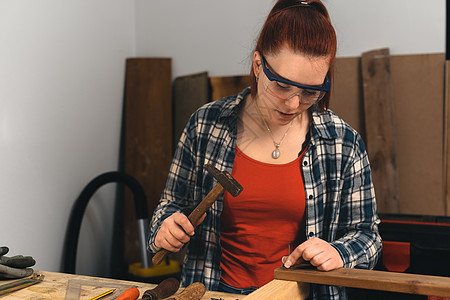 红头发的年轻女人 木匠在她小木工店 把钉子敲到木板上家具红发职业员工商务人士眼镜材料制造业木头图片