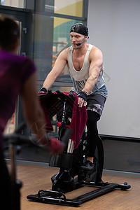 在自行车运动员训练师身上抽了一个自行车腿训练健身房合身 从健康和力量运动服的年轻健身 伙计 ike fat 白种人坚强的女人骑自图片