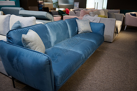 软装公司漂亮的极简主义时尚蓝色丝绒沙发 配有浅灰色枕头 在家具店陈列室出售 客厅配有时尚现代舒适的软垫家具背景