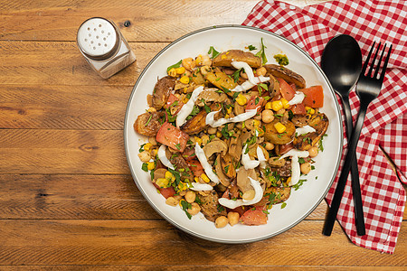 一份美味的土豆 鹰嘴豆 番茄和蘑菇沙拉 配欧芹和蒜泥蛋黄酱 放在木桌上的碗里 里面有叉子和勺子 健康 自制的纯素食品草药沙拉酱食图片