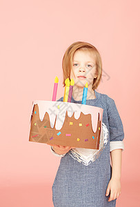 一个兴奋的漂亮小女孩的肖像 庆祝生日和展示蛋糕 在粉红背景上展露了蛋糕图片