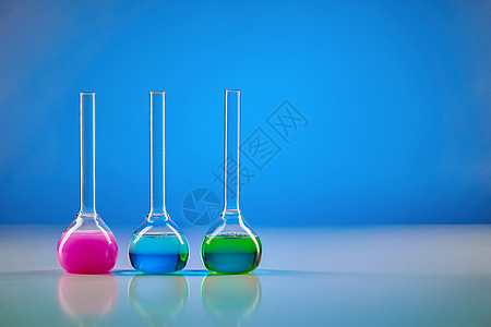 有五颜六色的化学试剂的三个医疗烧瓶为测试 蓝色背景 冠状病毒的实验室研究 大流行性 COVID-19 特写图片