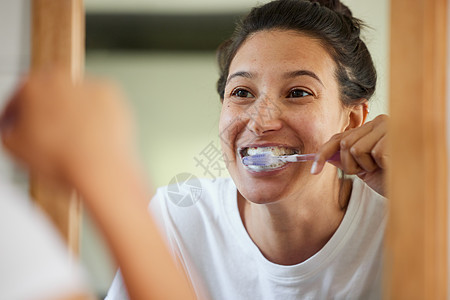 如果你想要健康的牙齿 你必须每天刷牙两次 一位年轻女子一边刷牙一边看着浴室镜子的镜头图片