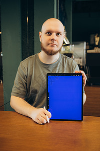 坐在现代咖啡馆附近的长椅上 快乐的男性用手指指着空白的平板电脑蓝屏药片酒吧屏幕街道工具媒体广告展示男人互联网图片