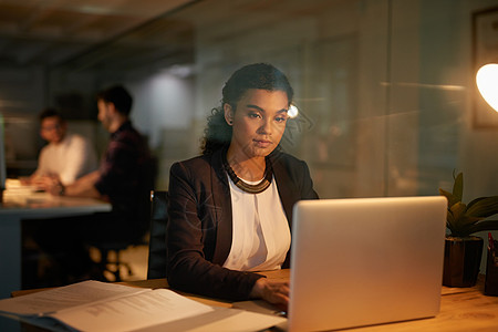 挑灯夜战 一位年轻女商务人士在办公室加班时使用笔记本电脑的镜头图片