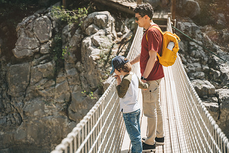 远足时 父子俩在山中的索桥上遥望 穿着随意的游客男童和他爸爸背着黄色背包穿过索桥穿过峡谷顶峰孩子公园男生悬崖环境穿越冒险父亲旅行图片