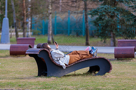 两个女孩躺在公园的晒日光休息员身上 下班后看电话 看看电话图片