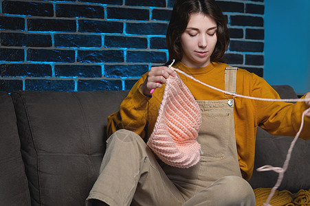 有吸引力的年轻女子坐在沙发上时编织羊毛衣 手织钩 家庭爱好生产天然羊毛制品钩针女性女士手指闲暇活动手工工艺纺织品快乐图片