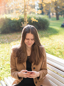 美丽的少女坐在公园的长椅上 拿着智能手机 在网上聊天 长头发的女人图片