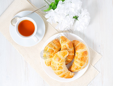 白桌上的茶杯 鲜花和新鲜烤面粉糕饼 最美味的羊角面包 顶层风景背景图片