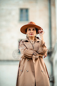 年轻优雅时尚的黑发女人的户外时尚肖像 模特戴着时尚的帽子 项链和轻雨衣在欧洲城市日落时摆姿势羊毛手腕衣服骆驼配件街道奢华手表毛衣图片