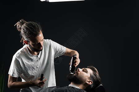在理发店刮胡子 长着脚镣的理发师修剪英俊胡子的男人黑色客户剃刀头发剪刀大男子主义剃须理发潮人图片