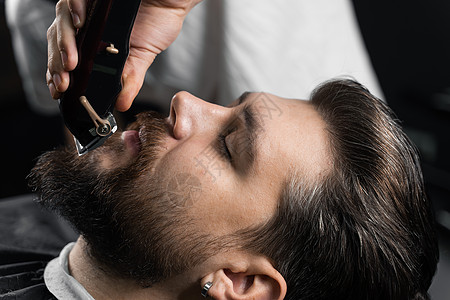 在理发店刮胡子 长着脚镣的理发师修剪英俊胡子的男人男性胡须工作室客户顾客黑色剃刀头发大男子剃须图片
