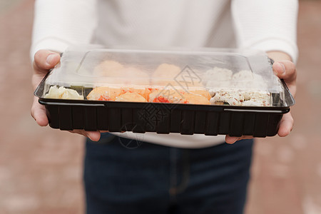 盒装健康食品配送在线服务中的特写寿司 穿白衣服的男人给你一套寿司 日本料理 面包卷 酱油 芥末外卖面具感染海鲜产品食物导游消毒防背景图片