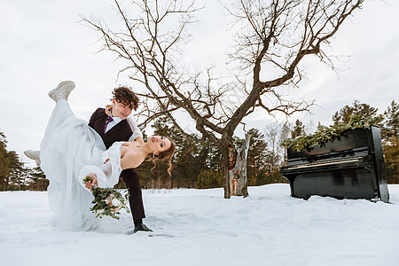 钢琴婚纱素材一个穿着婚纱的女孩和一个年轻男人 坐在雪中钢琴旁边化妆品乐器外套压痛爱情故事积雪派对女性婚姻男性背景