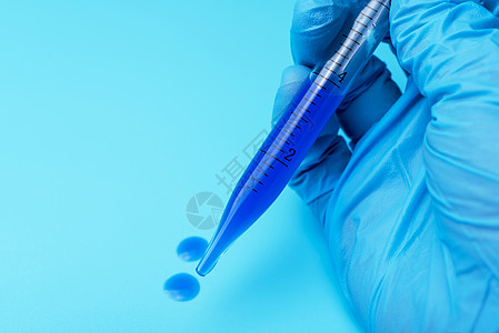 一只手套手拿着一个带蓝色液体的实验室管子图片