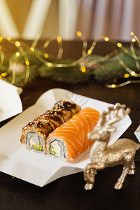 新年灯光背景上的寿司卷 圣诞灯装饰 除夕送外卖 与三文鱼 鳗鱼 鳄梨和软奶酪一起卷起来海苔菜单海鲜送货寿司盘海藻食物服务黄瓜背景图片