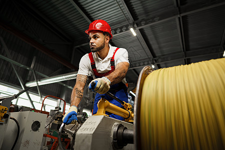 一名年轻的工厂工人卷起重型电线网圈金属工程线圈建筑布线工作工业电缆生产男性背景图片