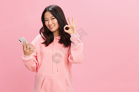 网路交流 亚洲学生快乐的年轻女士穿粉红连帽衫运动服展示好姿势 在粉红色工作室背景上被孤立 良好报价 Gadget成瘾社会媒体概念背景图片