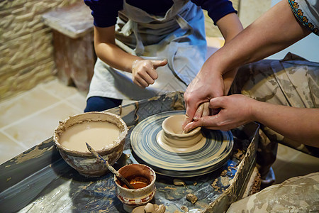 主人和学生的手在黄色粘土的波特车轮上做一个投手 有选择地集中注意力于手黏土杯子制品车轮工匠陶瓷陶器手指制造业雕塑家图片
