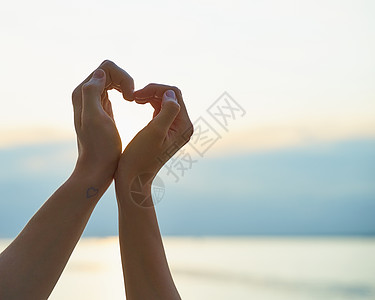 女性和男性的手露出心脏 爱的象征 海滩背景图片