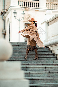 年轻优雅时尚的黑发女人的户外时尚肖像 模特戴着时尚的帽子 项链和轻雨衣在欧洲城市日落时摆姿势羊毛女士毛衣衣服奢华骆驼外套街道手表图片