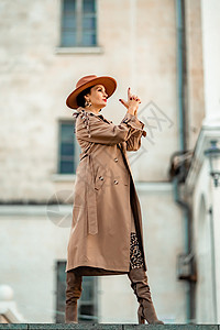 年轻优雅时尚的黑发女人的户外时尚肖像 模特戴着时尚的帽子 项链和轻雨衣在欧洲城市日落时摆姿势外套毛衣奢华手表羊毛手腕骆驼街道配件图片