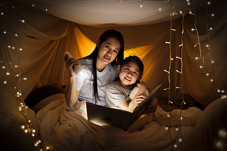 家庭观念 睡前 母亲和孩子的女儿在儿童帐篷里用手电筒一起看书 快乐的妈妈在床单帐篷里给女儿读故事书女性闲暇故事女孩学习阅读乐趣卧图片
