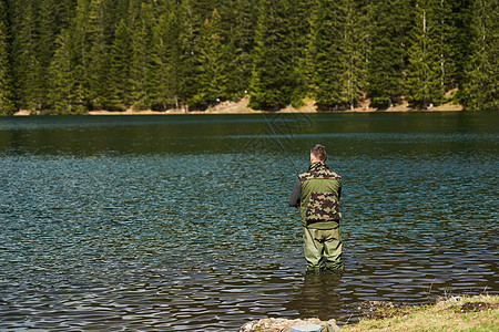 渔民站在水中 在湖里钓鱼 在山的深山背景上运动追求活动纺纱成人男性垂钓者淡水天空娱乐背景