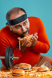 有胡子的中年男子 身着红色高领 头带 汉堡包和薯条 蓝背景 近距离 快餐冒充深色男人头巾食物肠胃桌子蓝色男性情绪图片