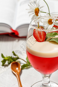 樱桃和牛奶果冻 加上玻璃中的草莓片和背景书籍图片
